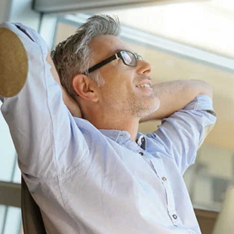 Foto eines Mannes mit weißem Hemd und Brille, der sich entspannt in seinem Stuhl zurücklehnt.